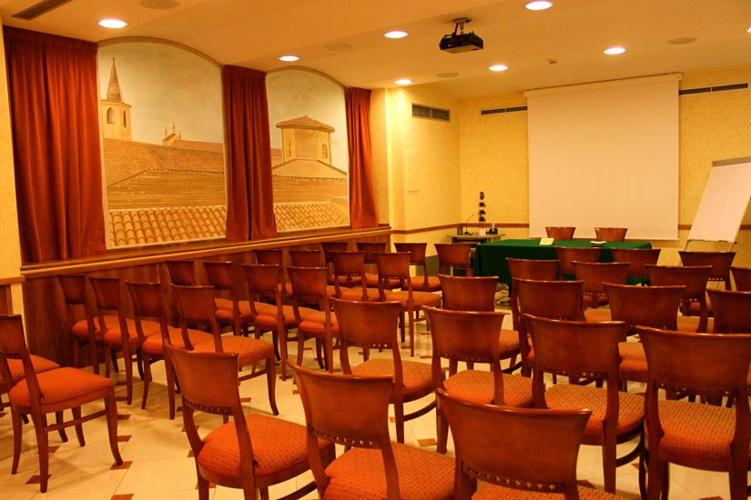 Sala riunioni allestita con file di sedie e schermo per proiezioni