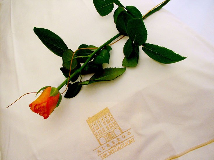 Una rosa posata su un tovagliolo ricamato con lo stemma dell’albergo